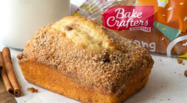 cinnamon crumb mini loaf on table top with cinnamon glass of milk and packaged loaf